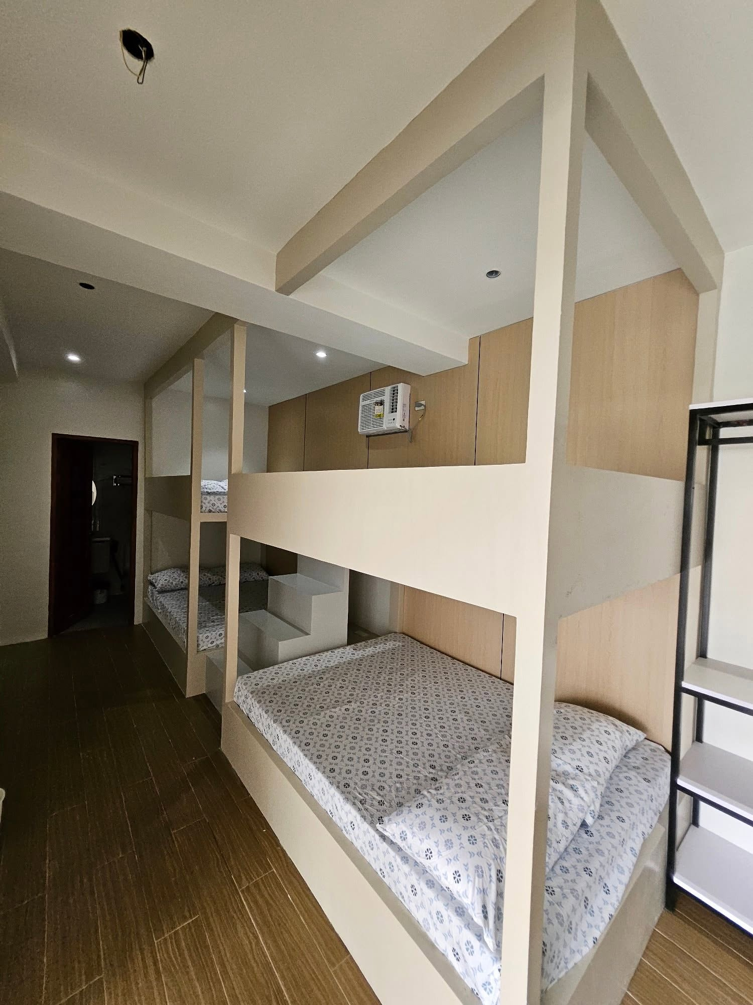 White built-in bunk beds, patterned bedding, an air conditioner and open shelving.