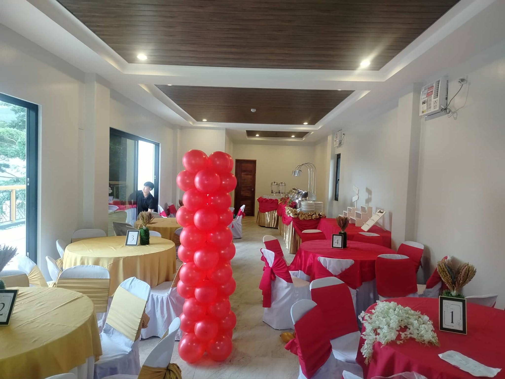 Red-and-gold table settings, covered chairs and a red balloon column inside the function room.