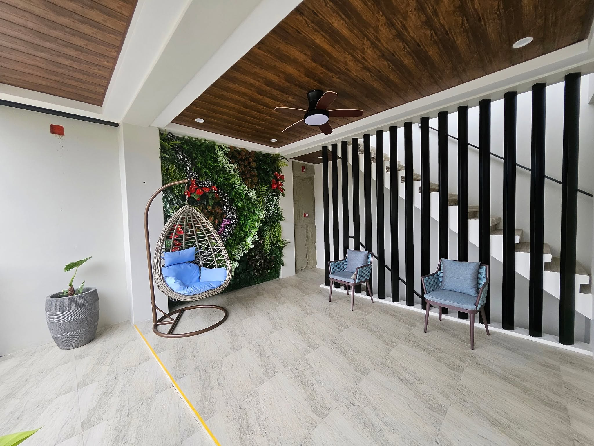 Hanging chair with blue cushions, two armchairs and a green feature wall beside the stairs.